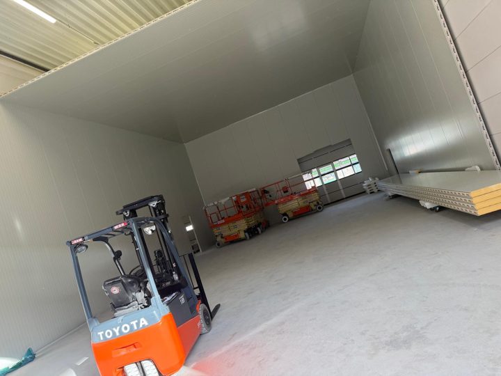 Leeres Kühlhaus aus weißen Paneelen in einer Halle, Gabelstapler im Vordergrund